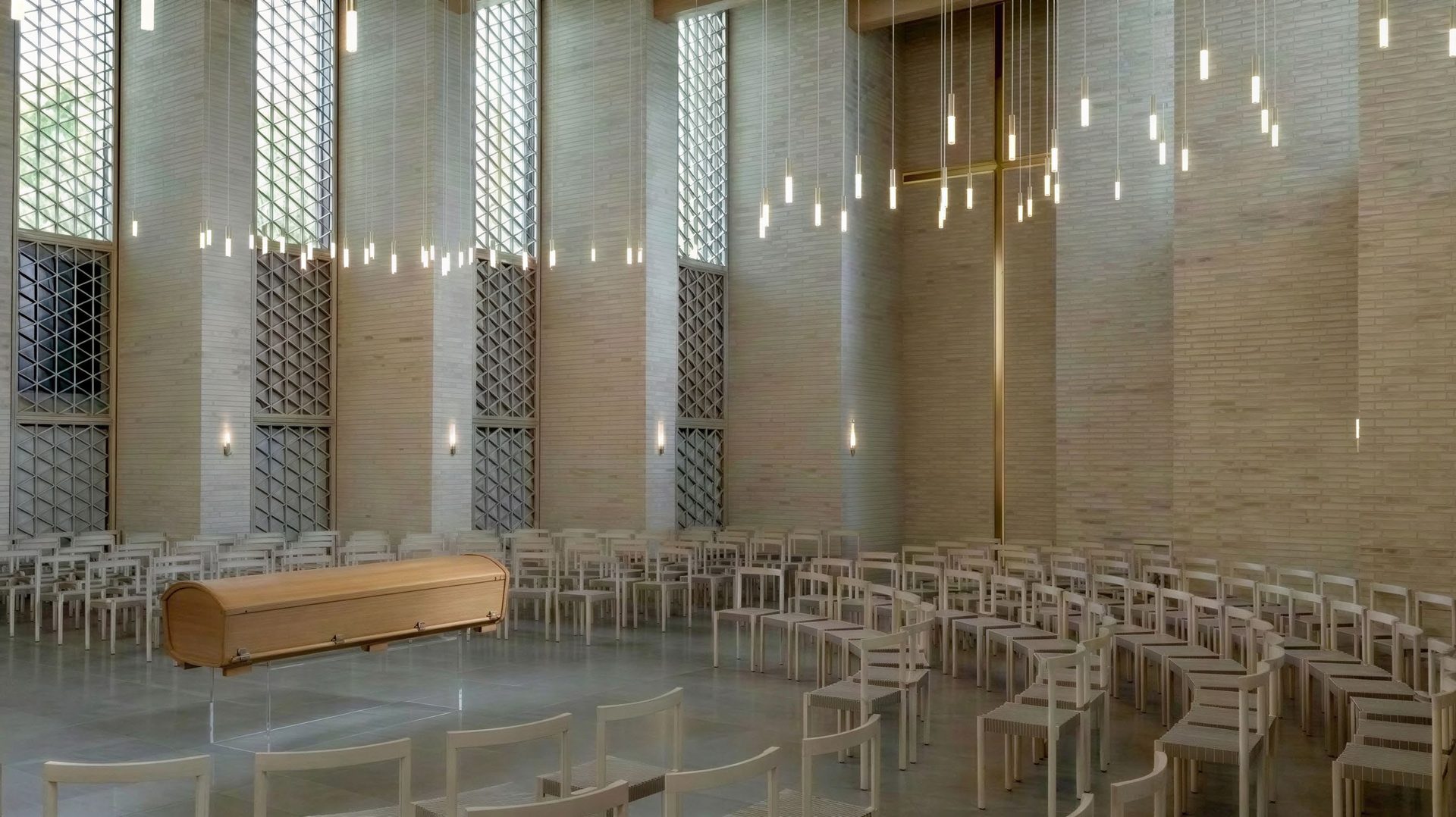 Ceremonirum med kista i ljust trä, stolar och hängande lampor